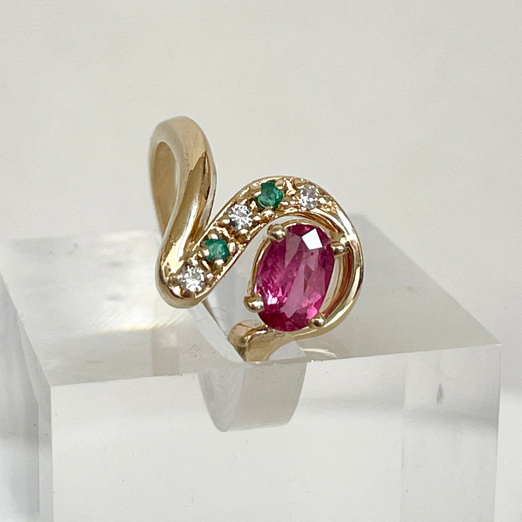 A vintage ring featuring a pink tourmaline center stone with a swirl design surrounded by diamonds and emeralds, set in a 14k gold band.